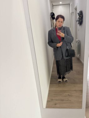 Koridorda poz veren bir kadın. Kırmızı bir kazağın üzerine ekose ceket giymiş. Tarz katmanları, kendini ifade etme ve günlük moda bireyselliği ve şehir yaşam tarzını yansıtıyor.