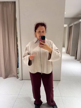 Deneme odasında montunu ayarlayan kadının yakın çekimi. Moda ve minimalist zarafetin dokunsal algısı ile dokunun keşfi, öz farkındalık ve kimlik