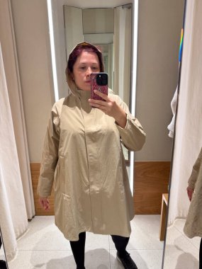 Aynada kapüşonlu bej bir yağmurluk deniyordum. Modern minimalizm ve yumuşak pratik tasarım ile ifade edilen koruma, adaptasyon ve bireysellik kavramı