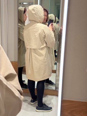 Bej yağmurluk giyen bir kadının arka görüntüsü. Modern konfor, sadelik ve sessiz güç fikri minimum dış giyim ve ince kentsel tasarım yoluyla