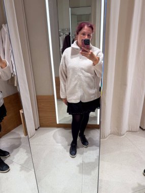 Kadın soyunma odasında beyaz yün ceket deniyor. Sıcaklığın, rahatlığın ve dokunsal algının minimum dokular ve kendini ifade etme yoluyla temsil edilmesi