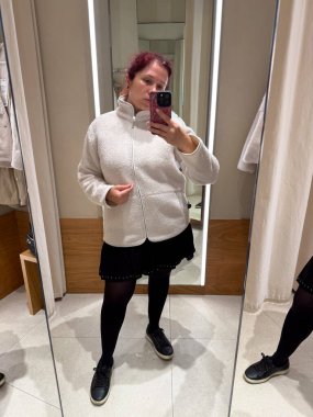 Deneme odasında montunu ayarlayan kadının yakın çekimi. Moda ve minimalist zarafetin dokunsal algısı ile dokunun keşfi, öz farkındalık ve kimlik