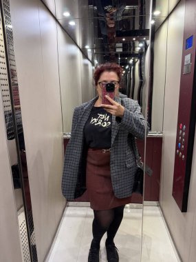 Asansörde aynalı selfie çeken bir kadın ekose ceket giyiyor. Kentsel kendini ifade kavramı, modern güven ve yansıtıcı mimari ortamda görsel simetri