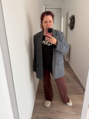 Bir kadın, evde ekose ceketli, günlük kıyafetleriyle selfie çekiyor. Orijinalliğin, konforun ve modern günlük kendini ifade etmenin temsili