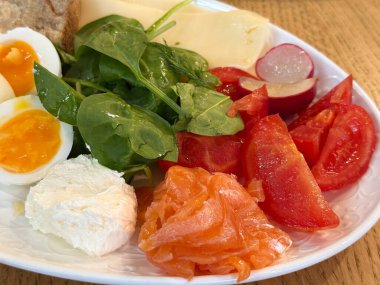 Sabah yemeği için domates, turp, ıspanak, peynir ve somon tabağı. Taze besin bileşimi sağlık ve mutfak dengesini sembolize ediyor