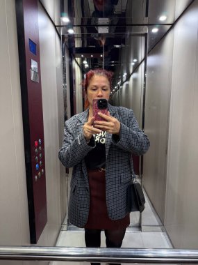Asansörde aynalı selfie çeken bir kadın ceket ve etek giyiyor. Yansıma ve bireysellik yoluyla kendini ifade etme, tarz ve modern şehir yaşam tarzı