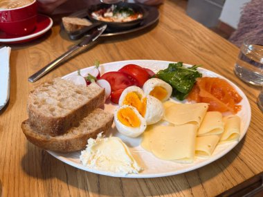 Beyaz tabakta haşlanmış yumurta, ekmek, yeşillik, peynir, somon ve domatesle sabah yemeği. Beslenme ve tazeliği temsil eden dengeli bir kahvaltı.