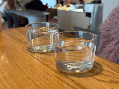 Ahşap kafe masasında iki bardak su. Sosyal yemek ortamında basitlik, susuzluk ve sakin atmosfer