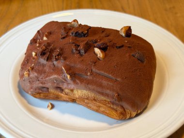 Beyaz tabakta fındıklı çikolata kaplı pasta. Tatlılık, doku ve sanatsal tatlı sunumunda hoşgörü