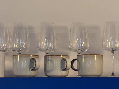 Mavi rafta seramik bardaklar ve şarap bardakları var. Mutfak iç mimarisi, minimalist organizasyon ve şekillerin, materyallerin ve yansımaların estetik uyumu