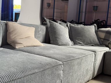 Parlak oturma odasında yastıklı modern gri kadife kanepe. Rahat iç mekan, rahat oturma alanı ve gevşemeyi ve minimalizmi vurgulayan yumuşak doku