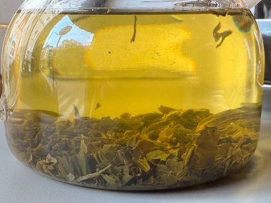 Cam çaydanlıkta demlenen çay yapraklarının yakın çekimi. Bitkisel karışım, doğal doku ve şeffaf sıcaklığın ayrıntıları.