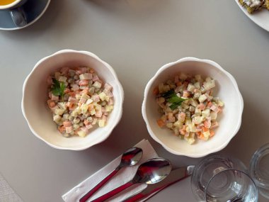 Kafe masasında iki kase Olivier salatası. Ortak yemek, aşçılık geleneği ve klasik ev yapımı mutfak yoluyla ifade edilen kültürel nostalji.