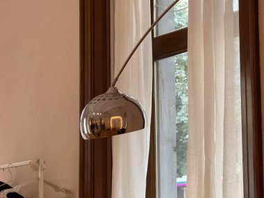 Pencerenin yanındaki yumuşak gün ışığında metal zemin lambası. Modern tasarım, sadelik ve sakin ortam çağdaş iç hayat tarzını yansıtıyor