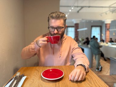 Adam şık bir kafede kahvesini yudumluyor. Sabah molasında lezzet, aroma ve dikkatli bir zevk anı.