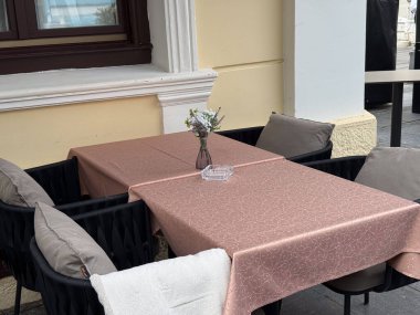 Açık kahve masası, pembe masa örtüsü ve çiçek vazosu. Rahat şehir terası, rahatlama ve sokak yemekleri atmosferi.