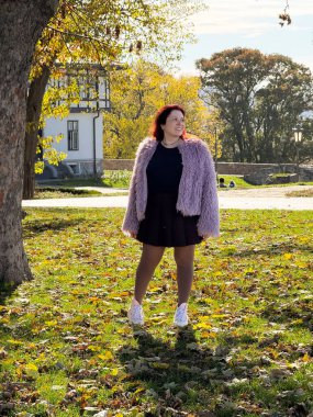 Ağacın yanında poz veren kadın sonbahar yapraklarıyla çevrili. Kendini ifade etme, iç denge ve doğayla barışçıl bağ.