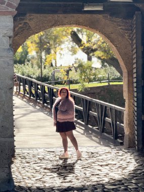 Güneşli bir günde taş kemerin altındaki kadın. Tarihsel park ortamında sonbahar atmosferi, eğlence ve keşif