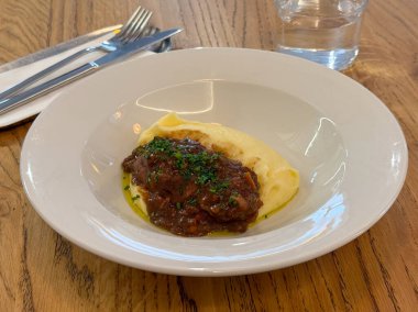 Tahta masadaki beyaz kasede servis edilen patates püresiyle sığır eti güveci. Boeuf bourguignon. Rahatlatıcı yemek..