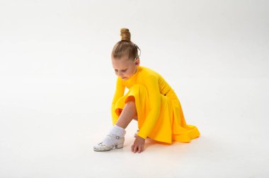 Koklear implantı olan küçük bir dansçı beyaz zemine ayakkabı ayarlıyor. Erken çocukluk sanatında işitme teknolojisine kapsama, disiplin ve farkındalık