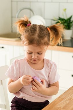 Mutfakta çikolata paketini açan genç bir kızın yakın plan portresi. Çocukluk konsantrasyonu, farkındalık ve günlük hayatta küçük keşiflerin neşesi.