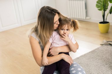Anne pencerenin yanında kızını öpüyor ve kucaklıyor. Sevgi, güven ve her gün aile şefkati ve sevgi ile nazik bir bağ.