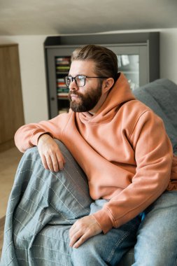 Düşünceli bir ifadeyle koltukta oturan adam. İç gözlem, yalnızlık, günlük rutin ve sıcak iç atmosferde zihinsel odaklanma kavramı