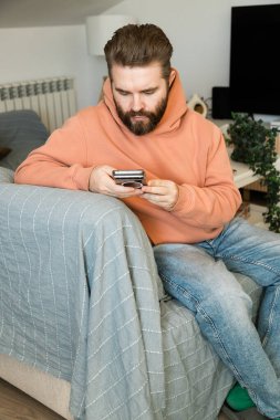 Evdeki koltukta akıllı telefon kullanan bir adam. Boş zamanlarında dijital etkileşim, teknoloji bağımlılığı, odaklanma ve iletişimi ifade eden modern iç rutin