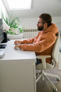 Parlak odada bilgisayarla çalışan bir adam. Ev ofisi kavramı, konsantrasyon, verimlilik ve modern dijital çalışma alanı yaşam tarzı