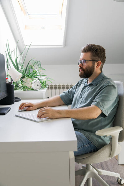 Man working at computer desk under skylight. Representation of focus, productivity, and modern remote work routine in bright home office environment