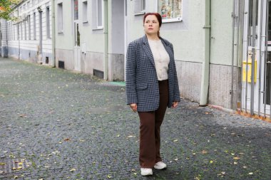 Ambar taşı caddesinde binaların yanında duran bir kadın. Sonbahar havası, yansıma ve sakin şehir yalnızlığı.