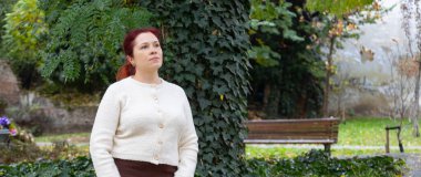 Bahçedeki sarmaşık kaplı duvarın yanında duran kadın. Fotokopi alanı olan pankart. Uyum, yansıma ve doğayla olan bağın sessiz olduğu bir anda