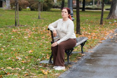 Yağmurlu bir sonbahar gününde parkta bankta oturan bir kadın. Sakin ruh hali, tefekkür ve günlük sadelik..