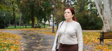 Sonbahar parkında yaprakları dökülmüş bir kadın. Reklam için yer ve boş yerleri kopyalayın. Farkındalık, mevsimsel sakinlik ve sessiz yansıma