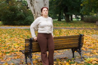 Sonbahar parkında bankta oturan bir kadın. Reklam için yer ve boş yerleri kopyalayın. Dinlenme, yansıma ve günlük farkındalık