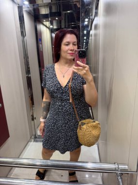 Asansörün içinde sıradan yaz kıyafetiyle selfie çeken bir kadın. Günlük rutinde modern yaşam tarzı, özgüven ve bireyselliğin ifadesi