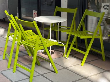 Canlı yeşil sandalyeler ve güneş ışığında vitrinin yanındaki beyaz masa. Açık hava ortamının eğlenceli rengi, kontrastı ve enerjisi