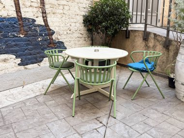 Yuvarlak masa ve açık kafedeki duvarın yanında yeşil sandalyeler. Bitkilerle, sadelikle ve sıradan yemek havasıyla rahat bir şehir terası.