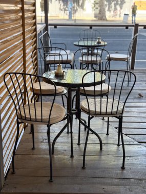 Sokakta sandalyeleri ve masaları olan küçük bir kafe terası. Açık hava oturma alanında sosyal etkileşim, konukseverlik ve sakin kentsel yaşam tarzı