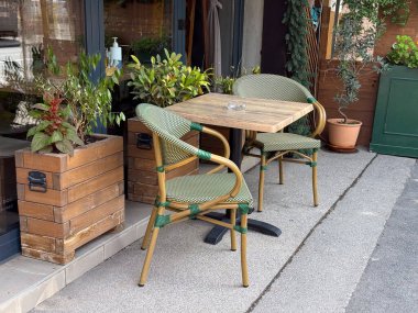 Yeşil sandalyeli ve saksı bitkilerli ahşap kafe masası. Şehir yemekleri, rahat atmosfer ve küçük sokak kafesi yaşam tarzı.