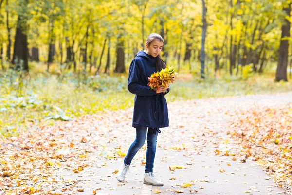 Счастливая девушка гуляет в осеннем парке с кленовыми листьями — стоковое фото