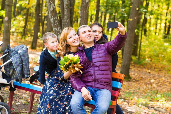 Família, infância, estação, tecnologia e conceito de pessoas - família feliz tirando selfie com smartphone no parque de outono — Fotografia de Stock