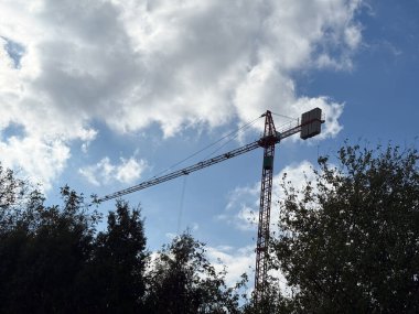 Mavi gökyüzünün altındaki ağaçların üzerinde turna. Sanayi gücü, ilerleme ve inşaat sembolizmi ile yakalanan sürekli şehir büyümesi.