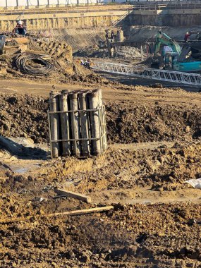 Güneş ışığı altında kazı alanındaki destek yığınları ve inşaat işçileri. Mühendislik altyapısı, kentsel kalkınma, el işçiliği aşaması ve temel gelişimi