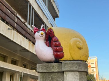 Mavi gökyüzünün altında beton kaidede duran yay ile oyuncu salyangoz heykeli. Kaprisli sokak sanatı, canlı dekorasyon, neşeli şehir ayrıntıları şehir alanına cazibe ve karakter getiriyor.
