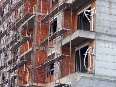 Gelişmekte olan bir binanın iskelesi ve tuğla duvarları yakından görülüyor. İnşaat aşaması, mimari çerçeve, tamamlanmamış yapı, ilerleme, mühendislik ve kentsel büyüme