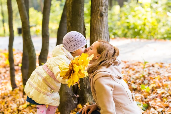 Мама целует свою дочь в парке. Женщина с ребенком в осеннем лесу . — стоковое фото