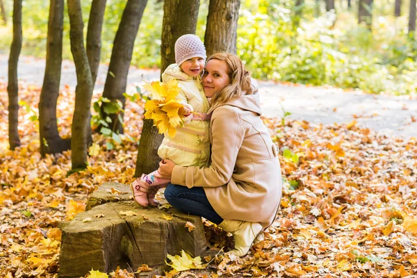 Mother kissing her daughter in the park.  Woman with child on autumn forest.