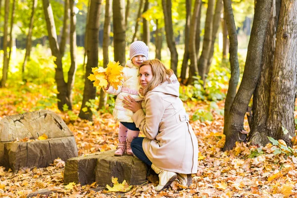 Mother kissing her daughter in the park.  Woman with child on autumn forest.