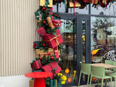 Noel hediyesi, kafe girişini paketlenmiş kutular ve sonsuza dek yeşil çelenklerle süsleme. Şenlikli şehir konukseverliği, mevsimlik pazarlama, tatil atmosferi, kış kutlaması ve kamu alanındaki tüketici sevinci